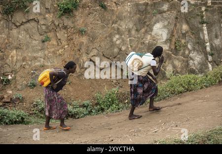 Two woman carry heavy water canisters on their backs from the water point to the village, near the village of Konso, southern Ethiopia Stock Photo