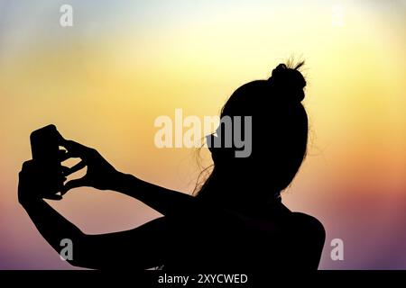 Silhouette of girl with smartphone taking selfie in the summer during the sunset Stock Photo