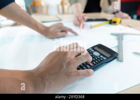 Engineer Working on Blueprint with Calculator and Tools in Office Setting Stock Photo