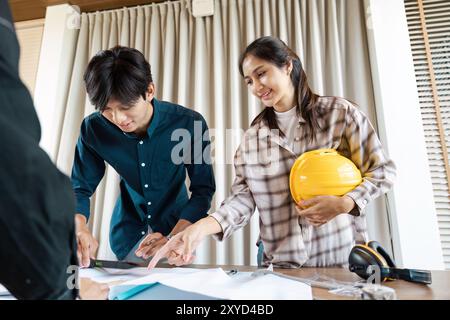 Young Engineers Collaborating on a Project with Blueprints and Safety Gear in a Modern Office Setting Stock Photo