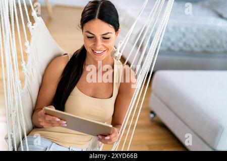 Social media time. Staying in touch with her tablet. Woman sitting on couch using tablet pc at home Stock Photo