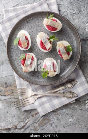 Scandinavian Devilled egg with beetroot and herring close-up in a plate on the table. Vertical top view from above Stock Photo