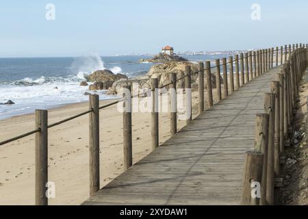 Boardwalk on the sandy beach, in the background the Capela do Senhor da Pedra, historic chapel on a rock at Praia do Senhor da Pedra, Gulpilhares, Vil Stock Photo