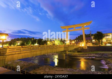 Large torii gate stands at end of Miyamae-bashi bridge spanning Miya-gawa river during blue hour at dusk in Hida-Takayama, Gifu Prefecture, Japan, Asi Stock Photo