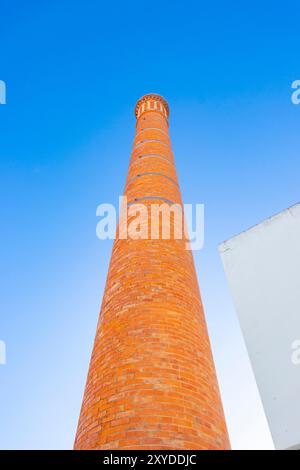 looking up at Tall red brick chimney stack against a clear blue sky with a partial white building on the right side. albufeira portugal Stock Photo