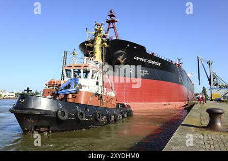 The oil tanker Unique Guaridan is towed in the harbour basin by a tugboat. Oil tanker towaged in harbour Stock Photo