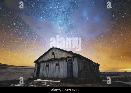 Night winter landscape. Abandoned wooden house against the background of the night starry sky in bright colors and sunset. The concept of travel and h Stock Photo