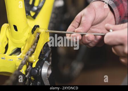Close-up maintenance of a mountain bike. Male hands adjust the chain tension. Technical condition monitoring in the workshop Stock Photo