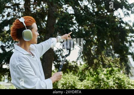 A woman wearing headphones films with a selfie stick in a campus setting. Stock Photo