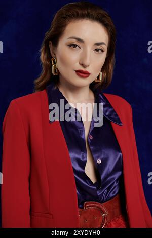 A stylish and attractive Asian woman poses in a red suit and silk shirt against a dark background. Stock Photo