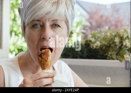 Woman bites into a freshly grilled chicken thigh Stock Photo