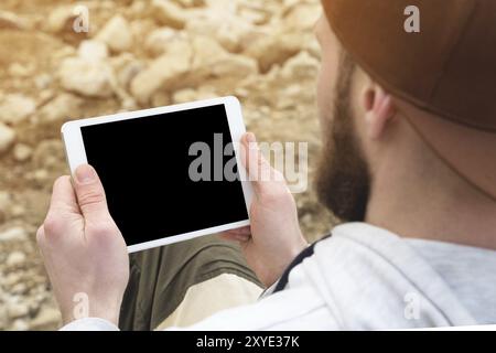 Close-up of a horde in a brown cap in the open air holds a white tablet pc in his hands. A bearded man looks at the tablet. OTS view from behind the s Stock Photo