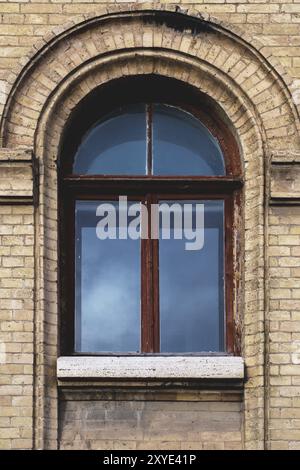 Vintage arched window in the wall of yellow brick. Black glass in a maroon dark red wooden frame. The concept of antique vintage architecture in build Stock Photo