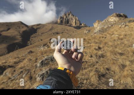 A male Hiker is looking for a direction with a magnetic compass in the mountains in the fall. Point of view shot. Man's hand with a watch bracelet hol Stock Photo