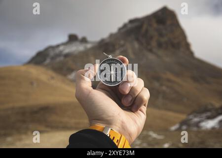 A male Hiker is looking for a direction with a magnetic compass in the mountains in the fall. Point of view shot. Man's hand with a watch bracelet hol Stock Photo