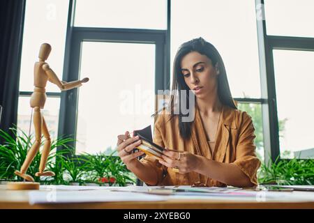 A Middle Eastern woman in a modern office thoughtfully examines a color palette, surrounded by design elements. Stock Photo