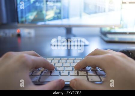 Hands are typing on a white keyboard, screen in the blurry background Stock Photo