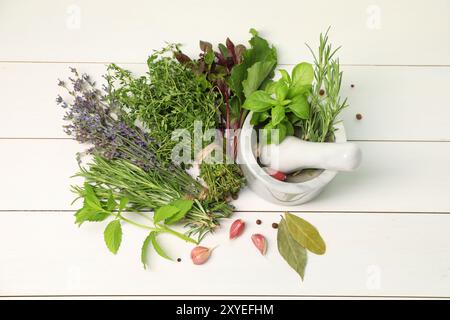 Different aromatic herbs, garlic, mortar and pestle on white wooden table, top view Stock Photo