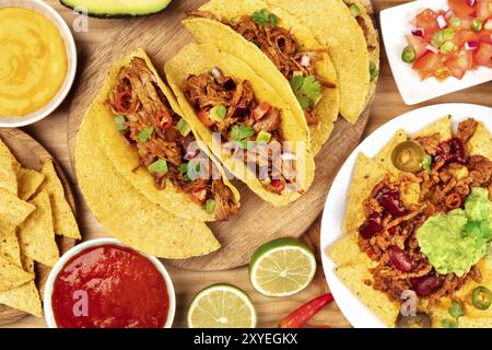 A photo of Mexican food, including tacos, guacamole, pico de gallo, and nachos with chili con carne, shot from the top with ingredients on a wooden ba Stock Photo