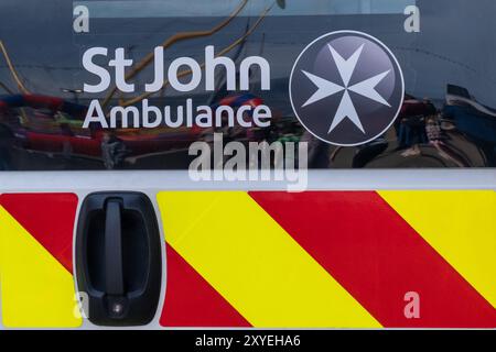 Rear of ambulance vehicle marked with St John logo and Maltese Cross with red and yellow chevron. Ballycastle, UK - August 24th, 2024: Stock Photo