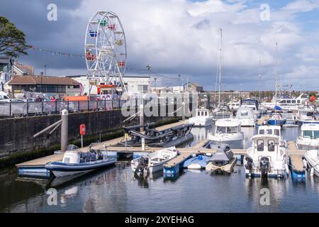 View of harbour, boats, yachts and Ferris Wheel set against cloudy sky on summer's day. Ballycastle, UK - August 24th, 2024. Stock Photo