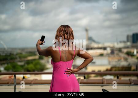Dauntless Black woman taking selfies on the rooftop of a Dallas hotel. She is wearing a fashionable pink sundress holding her phone up and out. Stock Photo
