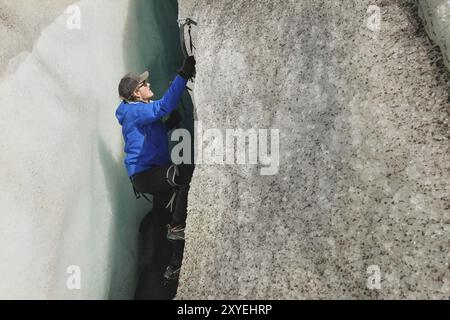 A free climber without insurance with two ice axes rises from a crack in the glacier. Free climbing without ropes Stock Photo