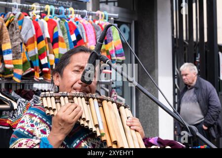 Man in colourful top playing South American wooden musical pipes on street. Ballycastle, UK - August 26th, 2024: Stock Photo