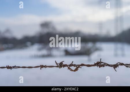 Barbed wire in the foreground in front of a hut with trees Stock Photo