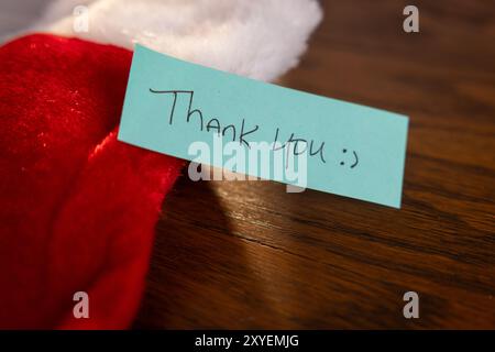 A blue note with the words "Thank You" written on it is placed on top of a red Santa Stalking. Stock Photo