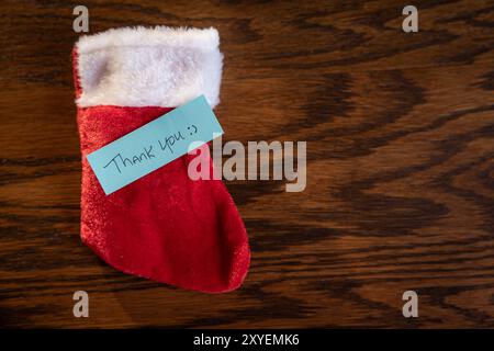 A blue note with the words "Thank You" written on it is placed on top of a red Santa Stalking. Stock Photo