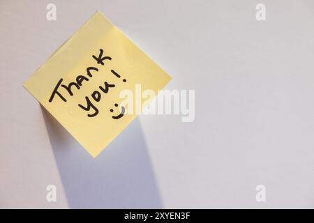 A yellow sticky note with the words "thank you" written on it. The note is taped to a wall or a surface Stock Photo