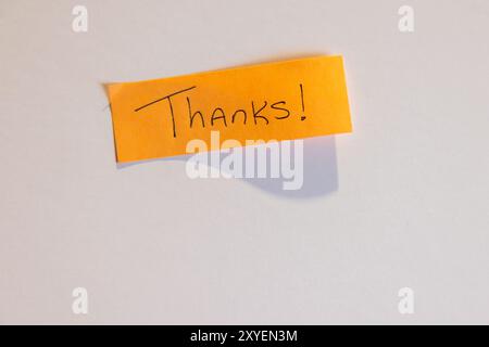Orange sticky note with the word "thanks" written on it. The note is taped to a white wall or a surface Stock Photo