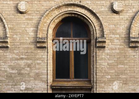 Vintage arched window in the wall of yellow brick. Black glass in a maroon dark red wooden frame. The concept of antique vintage architecture in build Stock Photo