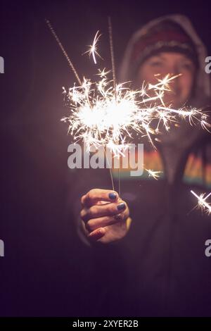 Smiling girl is holding a sparkler in her hand, new year, outdoors Stock Photo