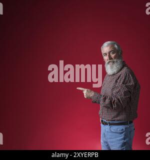 Senior man pointing his finger something against red background Stock Photo