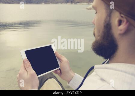 Close-up of a horde in a brown cap in the open air holds a white tablet pc in his hands. A bearded man looks at the tablet. OTS view from behind the s Stock Photo