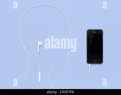 Man head outline made by a headphone cord plugged into iPhone 5s smartphone. Creative music concept on blue background Stock Photo