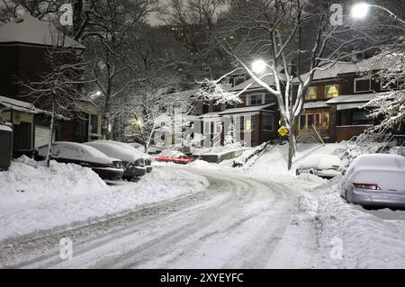 Covered with snow road illuminated with street lights at night And there is a glimpse of red light trails from a car that has just turned around the c Stock Photo
