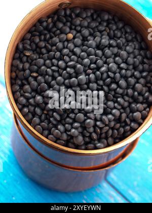 Beluga lentils in stacked copper bowls on a rustic blue kitchen table Stock Photo