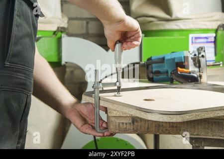 Close up Master clamps the workpiece with a dvp clamp to the workbench and on the background lies Carpentry hand router Stock Photo