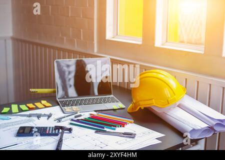 Engineers and architects' desk filled with blueprints, stationery and computers Equipment, stationery, a lot of documents and a helmet placed on the e Stock Photo