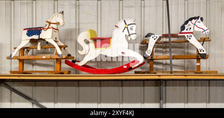 Three wooden rocking horses in a line on display in auction room, UK Stock Photo