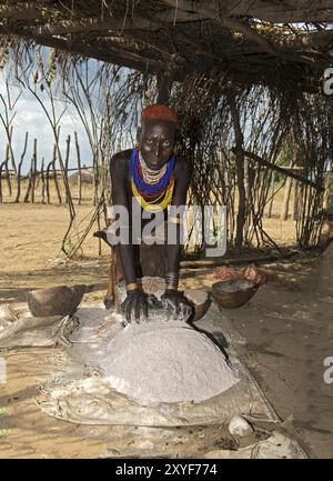 Woman from the Arbore ethnic group grinding red sorghum millet on a grinding stone, Southern Omo Valley, Ethiopia, Africa Stock Photo