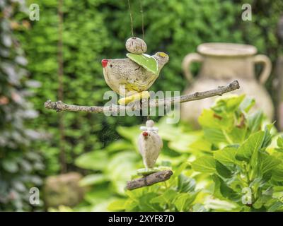 Two floating cartoon birds on a branch in the middle of a green garden with a rustic clay jug in the background, borken, muensterland, germany Stock Photo