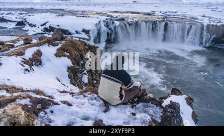 A man sitting looking at the frozen Godafoss waterfall at sunset in winter, Iceland, Europe Stock Photo