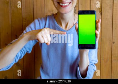 Smiling thin woman shows chromakey on smartphone screen. unrecognizable persona. Close-up. Soft focus, blurred. Stock Photo