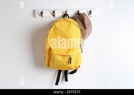 Yellow backpack and cap hanging on white wall Stock Photo