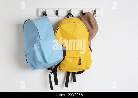 Bright backpacks and cap hanging on white wall Stock Photo