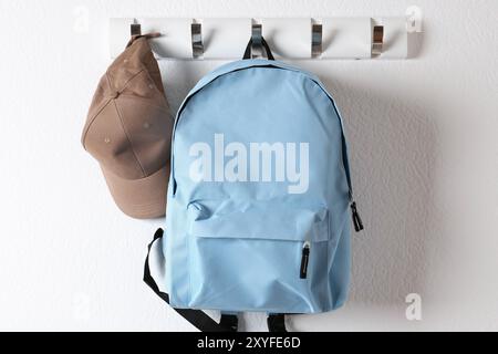 Light blue backpack and cap hanging on white wall Stock Photo